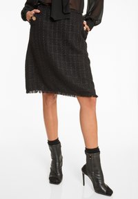 Schwarzer Tweedrock mit Karomuster, fransigem Saum und Taschen. Kombiniert mit schwarzen Peeptoe-Stiefeletten mit Reißverschlüssen und strukturierten Akzenten.