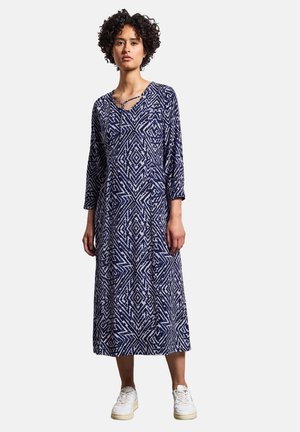Robe longue bleu marine avec un motif géométrique blanc, décolleté en V, et manches trois-quarts, en tissu doux, associée à des baskets blanches.