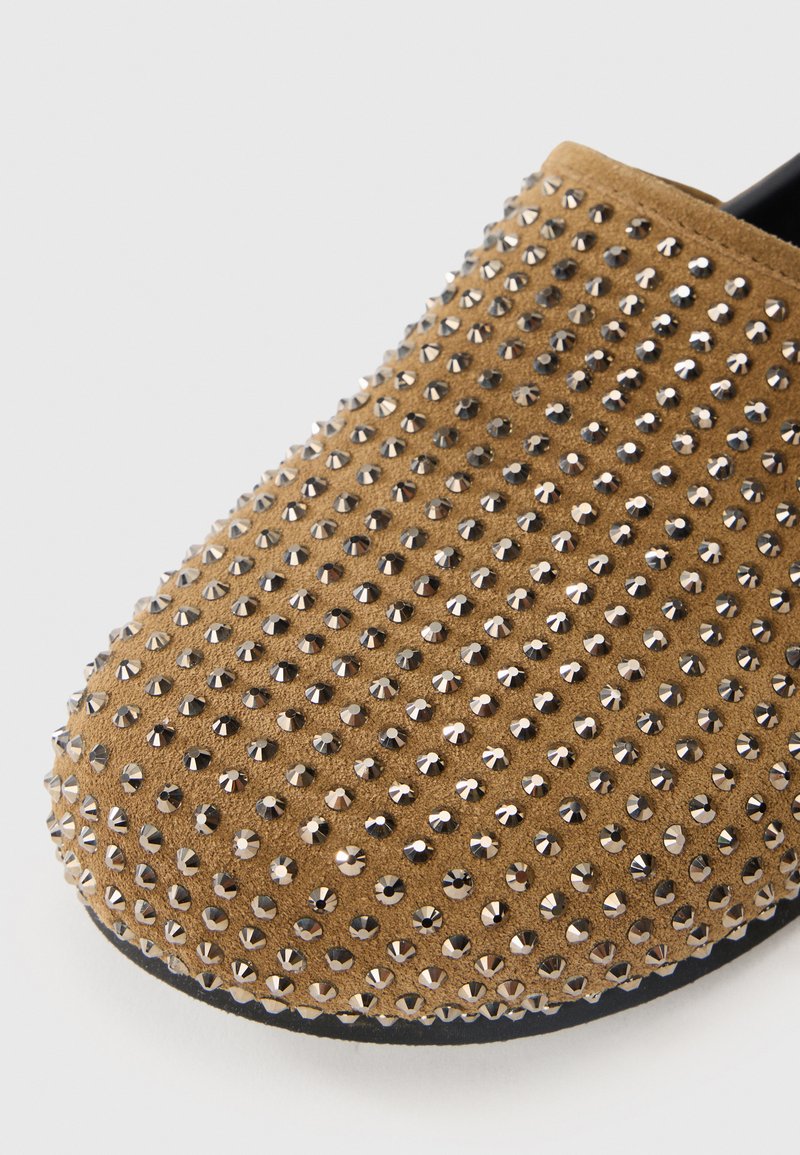 Braune Wildleder-Slipper mit silbernen Nieten, runder Zehenform und strukturiertem Obermaterial für ein auffälliges Design.