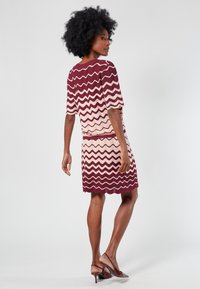 Knit dress with maroon and cream zigzag pattern, short sleeves, and ribbed hem. Paired with clear heeled shoes.