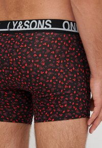 Boxer shorts neri con un motivo floreale colorato in rosso e rosa. Presentano un elastico in vita con il testo "Y&SONS" in grigio. Materiale leggero.