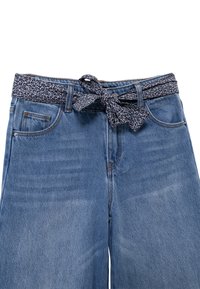 Pantaloni in denim blu con gamba ampia, dotati di una cintura di tessuto a fantasia scura annodata in vita. Tasche frontali e leggera usura visibile.