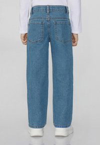 Světle modré džíny s volným střihem, s vysokým pasem, dvěma zadními kapsami a šitými detaily, v kombinaci s bílými teniskami.