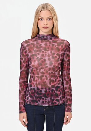 Giovane donna con lunghi capelli biondi che indossa un top aderente a maniche lunghe con stampa leopardata rosa e viola e jeans blu scuro.