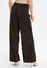 Pantalons en velours côtelé marron à jambes larges avec des côtes verticales, dotés d'une taille haute et d'une texture lisse. Associés à des talons de couleur claire.
