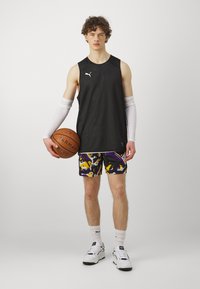 Camiseta deportiva sin mangas negra, pantalones cortos con un estampado colorido en amarillo y púrpura, mangas de brazo blancas y zapatillas de baloncesto en blanco y negro.