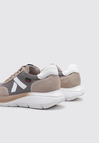 Zapatillas de ante y malla beige con acentos blancos, forma redondeada, suelas gruesas y un logotipo blanco prominente en el lateral.