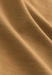 Primer plano de tela lisa de color marrón claro con textura fina de punto visible y pliegues suaves.