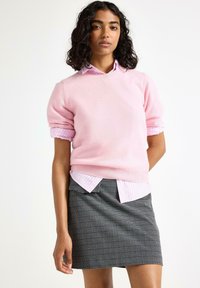 Lys pink striktrøje med korteærmer over en hvid og pink stribet skjorte, parret med en gråternet nederdel.