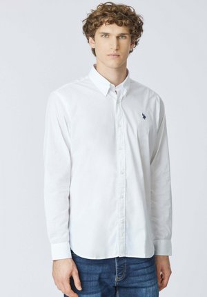 Camicia bianca a maniche lunghe con bottoni e colletto classico, con un piccolo logo blu navy sul petto, realizzata in tessuto di cotone liscio.