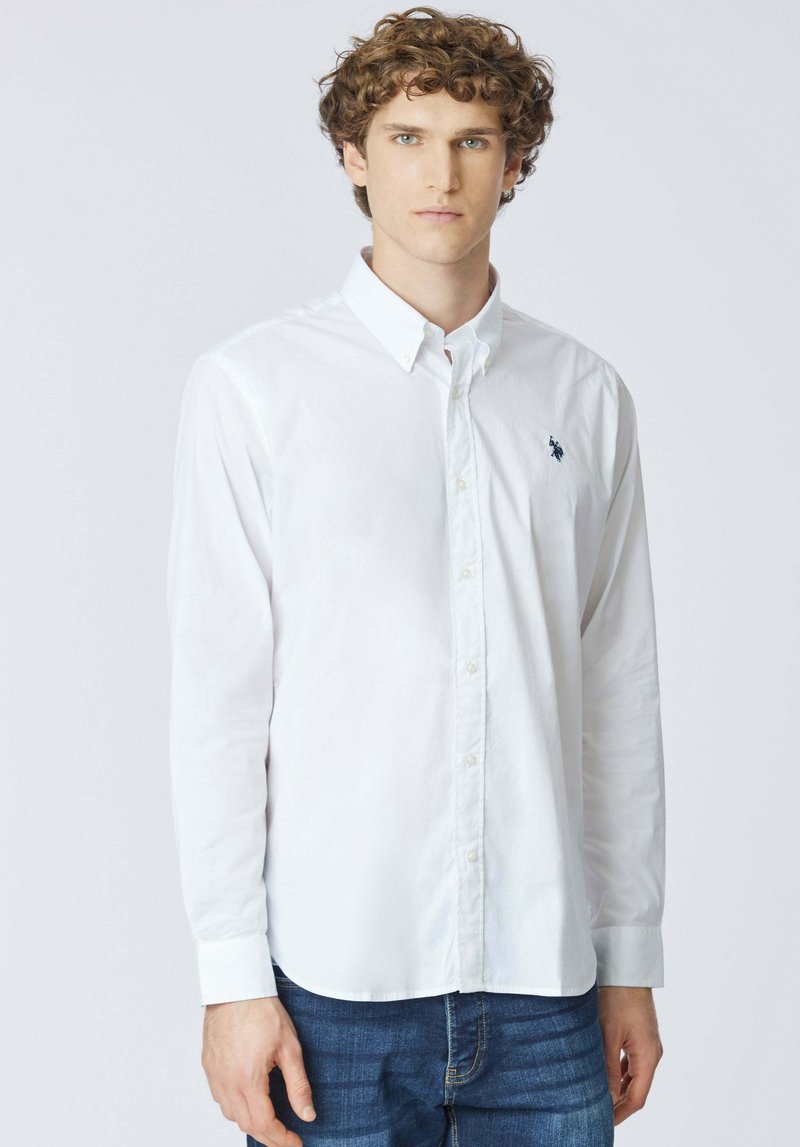Camicia bianca a maniche lunghe con bottoni e colletto classico, con un piccolo logo blu navy sul petto, realizzata in tessuto di cotone liscio.