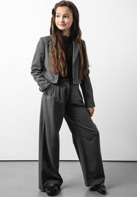 Szary garnitur w paski z krótką marynarką i szerokimi spodniami. Ubranie ma gładką teksturę i jest zestawione z czarnymi butami.