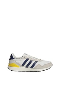 Baskets Adidas blanches et grises avec des bandes bleu marine et un accent jaune au talon, vues de profil sur un fond blanc.