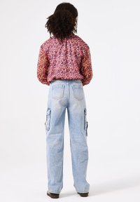 Blouse fleurie à manches longues, motif multicolore ; jeans cargo bleu clair avec poches latérales ; coupe décontractée ; portée avec des chaussures foncées.