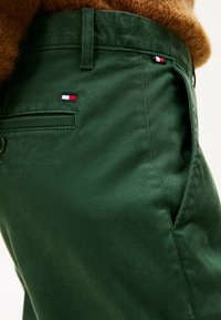 Zielone bawełniane spodnie charakteryzujące się gładką teksturą, tylną kieszenią oraz małym haftowanym logo w kolorach czerwonym, białym i niebieskim.