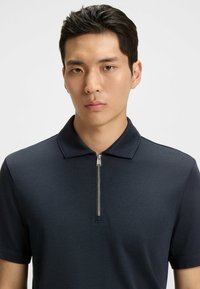 Mörk marinblå kortärmad polo t-shirt i texturerad tyg, med dragkedja i kragen och en avslappnad passform. Inga mönster eller detaljer.