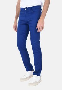 Jeans skinny in misto cotone blu con design a cinque tasche, chiusura frontale con zip e bottone, abbinati a sneakers bianche.