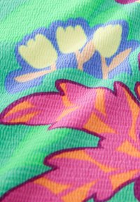 Textil mit einem leuchtend grünen Hintergrund, großen rosa und orangefarbenen Blättern sowie gelben Blumen, strukturiert mit sichtbarer Stoffwebung.