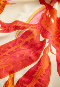 Motif floral abstrait rouge et orange sur tissu blanc lisse avec une texture soyeuse, montrant des plis et des reflets.