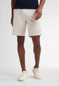 Lys beige bomulds shorts med en ret snit, sidelommer og en ren kant, parret med hvide sneakers, på en neutral baggrund.