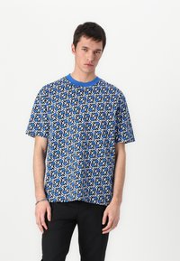 Blaues T-Shirt mit kurzen Ärmeln und geometrischem Muster in Weiß und Schwarz. Mit Rundhalsausschnitt und lockerer Passform, aus weichem Stoff gefertigt.