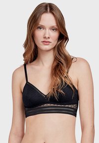 Bralette en dentelle noire avec un décolleté en V doux, des bretelles ajustables et une bande transparente avec un motif en relief. Texture lisse avec un design délicat.