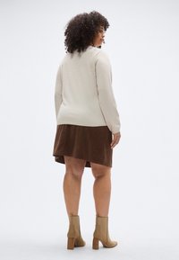 Beiger Pullover mit lockerem Schnitt, kombiniert mit einem braunen Cordrock mit asymmetrischem Saum und hellbraunen Stiefeletten mit klobigem Absatz.