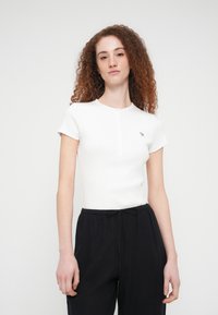 Λευκή μπλούζα με κοντά μανίκια και ραβδώσεις, σε στυλ henley με κεντρικό κούμπωμα και μικρό πράσινο λογότυπο στο αριστερό στήθος.