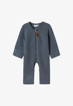 Sivý vlnený overal zo zmesi s dlhými rukávmi, predným zipsom a koženým úchytným pútkem. Má zaoblený výstrih a otvorený strih nohavíc.