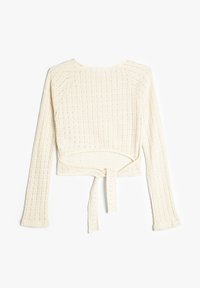 Crème-kleurige cropped trui met ribbelstructuur, lange mouwen en een strikdetail in de taille. Het materiaal lijkt zacht en gebreid.