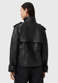 Zwart leren jas met een hoge kraag, schouderstukken en een gelaagde achterkant. Heeft gesps accents op de manchet en een slim fit.