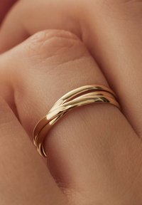 Drei ineinandergreifende goldene Ringe mit einer glatten, glänzenden Oberfläche, die an einem Finger vor einem strukturierten Hauthintergrund platziert sind.