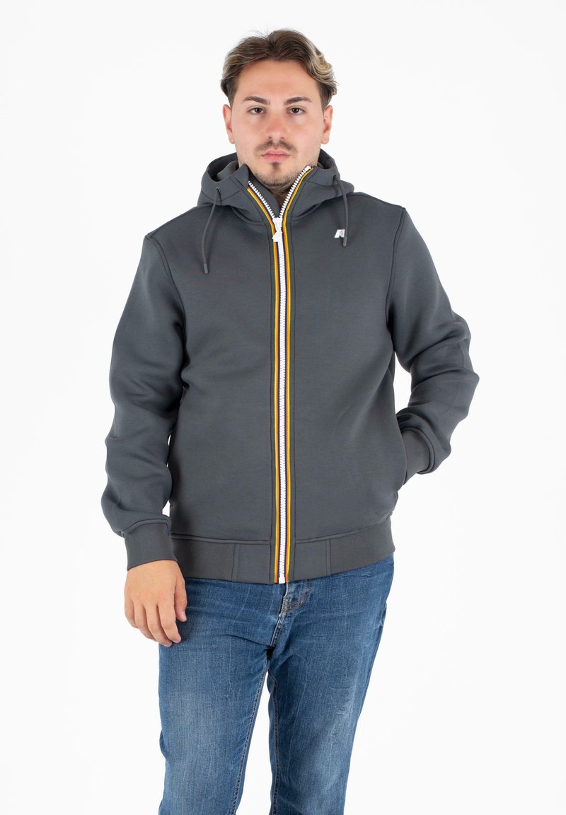 Grijze zip-up hoodie met een witte rits en gele en oranje accenten, voorzien van een capuchon, trekkoorden en ribbelboorden.