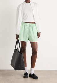 Zielono-białe paskowane szorty z elastycznym paskiem i detalem guzika, zestawione z białym krótkim topem i czarną torbą na ramię.
