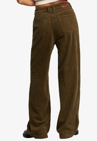 Corduroy wide-leg pants in dark olive green, featuring vertical ribbed texture, two back pockets, and a leather brand patch on the waistband.