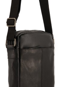 Sort læder crossbody taske med en struktureret finish, justerbar stofrem og en frontlomme med lynlås. Udstyret med sølvfarvede hardware detaljer.