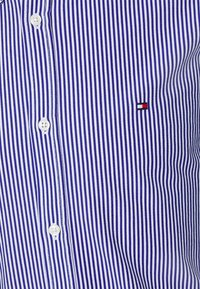 Blauw en wit gestreepte button-up shirt. Gemaakt van stof met een gladde textuur. Heeft een klein geborduurd logo in rood, wit en blauw.