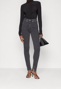 Svart långärmad topp med ruching framtill, kombinerad med höga, smala mörkgrå jeans med sidoklyftor vid anklarna och svarta klacksandaler.