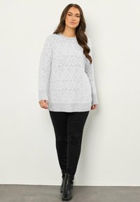 Jasnoszary sweter dzianinowy z teksturowanym wzorem, okrągłym dekoltem i ściągaczami na rękawach, w połączeniu z czarnymi spodniami slim-fit i botkami na kostkę.