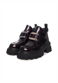 Bottines noires brillantes avec semelles épaisses, présentant une double sangle et de grandes boucles métalliques. Tige texturée avec une finition brillante.