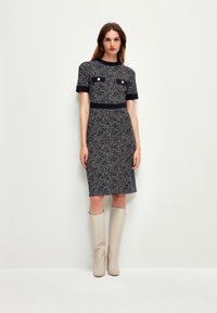 Vestido de tweed en azul marino y blanco con mangas cortas, dos bolsillos en el pecho y una silueta ajustada. Combinado con botas beiges hasta la rodilla.