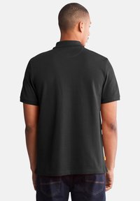 Black polo shirt with a straight-cut hem, short sleeves, and a classic collar. Smooth fabric with a subtle texture, no visible patterns.