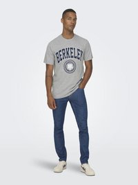 Šedé tričko s krátkym rukávom s nápisom "BERKELEY" a logom v námorníckej modrej farbe, spárované s tmavomodrými džínsami a bielymi teniskami.