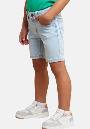 Shorts en denim bleu clair avec une coupe classique à cinq poches, dotés d'une fermeture à boutons et d'un léger délavage. Portés avec des baskets blanches aux accents orange.