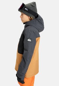 Schneejacke mit einem Farbabstufungsdesign in Grau, Schwarz und Orange. Ausgestattet mit einer Kapuze und einem verstellbaren Handgelenkbündchen.