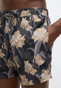 Plavkové šortky z čiernej látky s kvetinovým vzorom v béžovej a zelenej farbe. Majú elastický pás s šnúrkou a bočné vrecká.