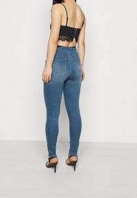Jeans de tiro alto en azul hechos de mezclilla, con un ajuste ceñido y dos bolsillos traseros. Combinados con un top corto negro de encaje y tacones altos.