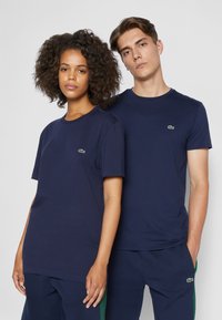 Navyblauwe katoenen T-shirts met ronde hals, met een klein groen Lacoste-logo op de linkerborst. Eenvoudig, onopgesmukt ontwerp.