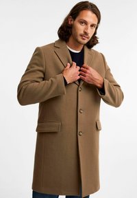 Brązowy płaszcz o strukturalnym designie, z dwiema przednimi kieszeniami i wykładanym kołnierzem. Posiada zapięcia na guziki oraz miękką, teksturowaną tkaninę.