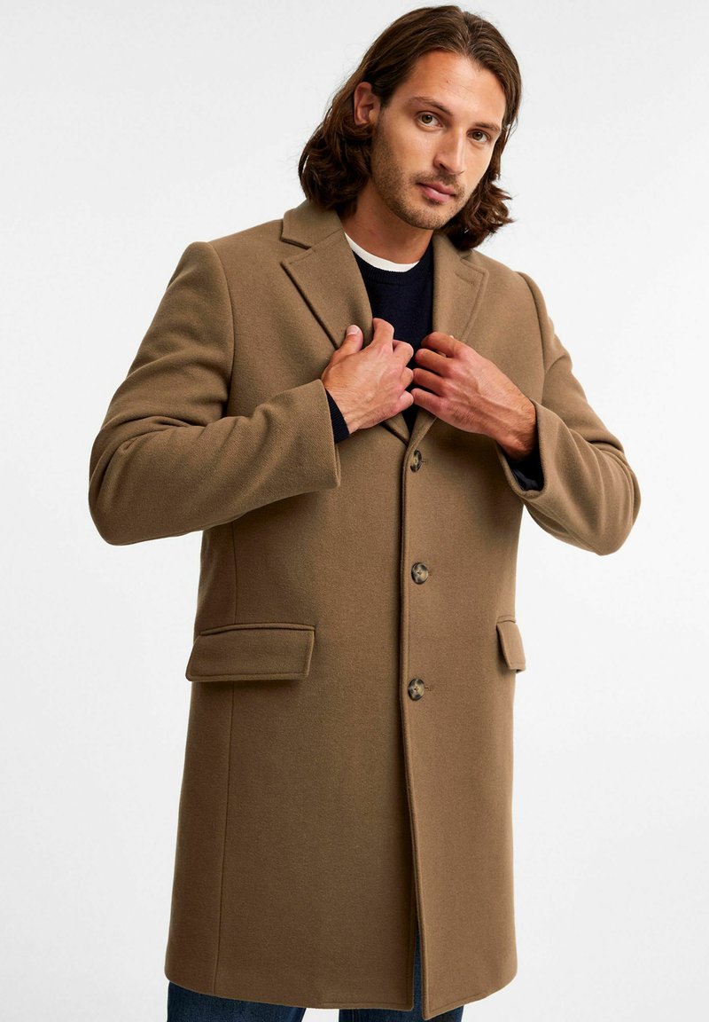 Brązowy płaszcz o strukturalnym designie, z dwiema przednimi kieszeniami i wykładanym kołnierzem. Posiada zapięcia na guziki oraz miękką, teksturowaną tkaninę.